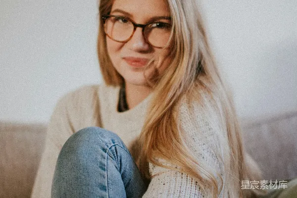 高清摄影 穿着蓝色牛仔裤和白色毛衣的女子坐在灰色沙发上。