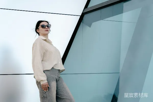 高清摄影 戴墨镜的女子站在一座现代几何建筑前。
