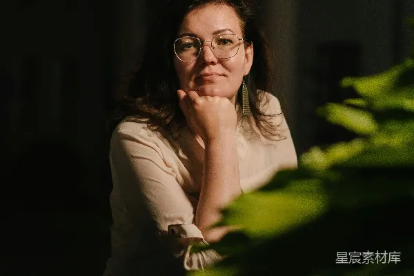 高清摄影 戴眼镜的女人坐在一盆植物前面。