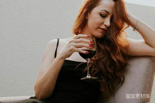 高清摄影 一位女士坐在沙发上，手里拿着一杯红酒。