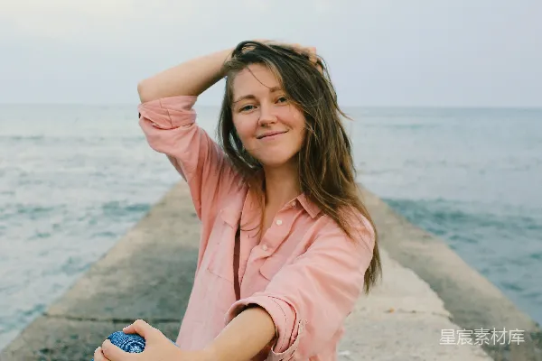 高清摄影 穿着粉色纽扣衬衫和蓝色牛仔裤的女人坐在灰色混凝土路面上。