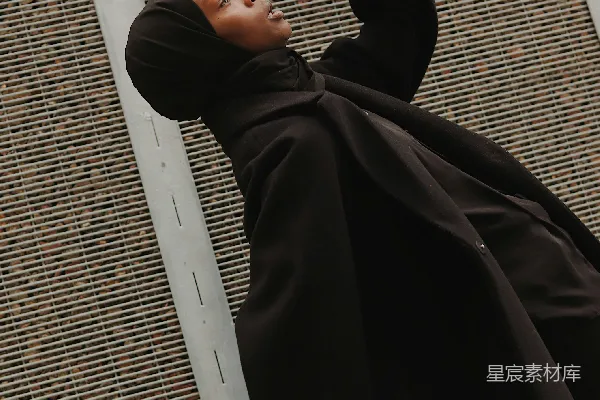 高清摄影 身穿黑色长袍的男人躺在白色金属杆上