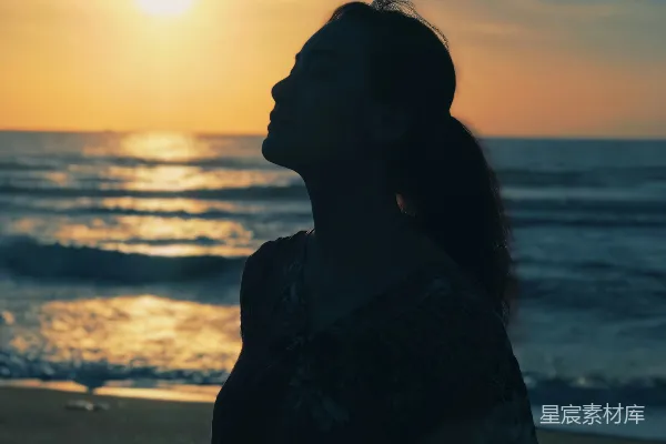 高清摄影 在日落时分，一个站在海滩上的女人的剪影。