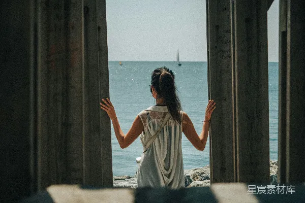 高清摄影 白天，一位穿着白色连衣裙的女子站在海滩上。