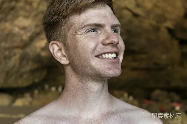 高清摄影 白天，一个赤裸的男子在棕色岩石形成的背景前微笑。