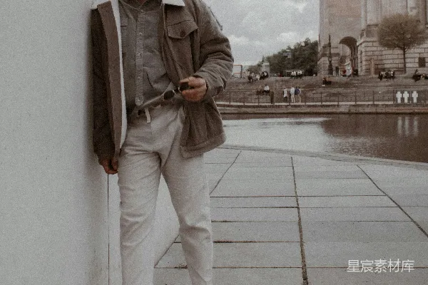 高清摄影 穿着灰色拉链夹克和白色裤子的男人站在灰色混凝土地板上，时间是白天。