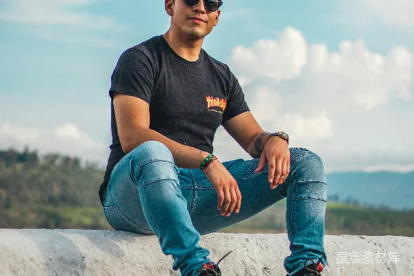 高清摄影 一个穿着黑色圆领T恤和蓝色牛仔裤的男人坐在灰色混凝土墙上。