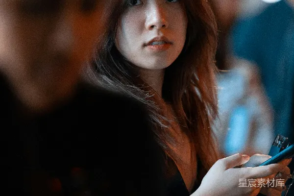 高清摄影 一个女人站在一个拿着手机的男人旁边。
