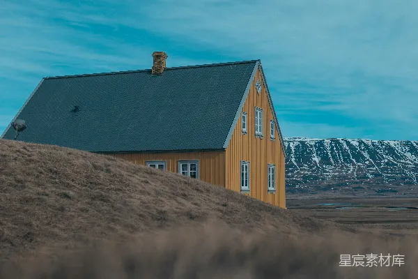 高清摄影 一座坐落在山丘上的黄色房子，背景是白雪覆盖的山脉。