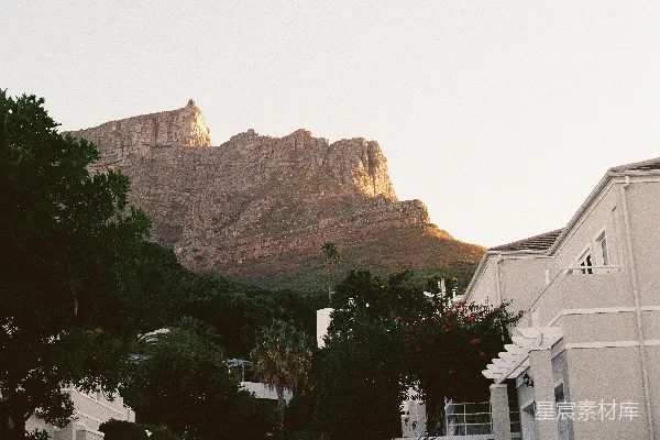 高清摄影 夕阳西下，一座大山矗立在建筑物后方。