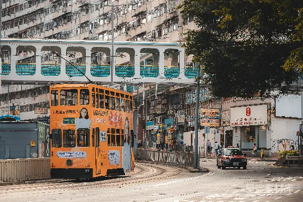 高清摄影 橙色的有轨电车行驶在街道上，两旁是建筑物和树木。