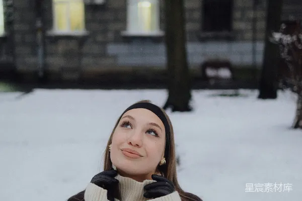 高清摄影 年轻的女子在黄昏时分的雪地庭院中抬头看。