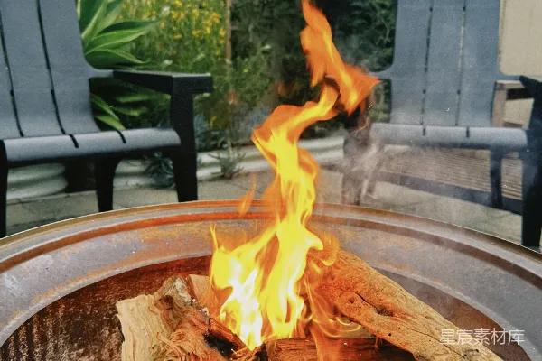 高清摄影 一个后院的篝火坑，里面燃烧着木头，旁边放着两把椅子。