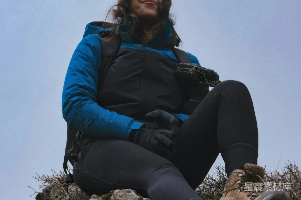 高清摄影 穿着徒步装备的女性坐在岩石上，手里拿着相机。