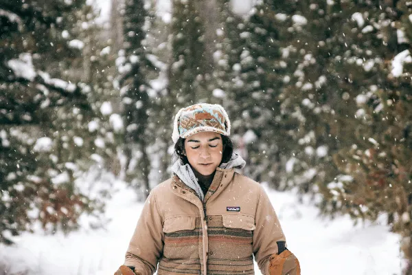 高清摄影 穿着棕色夹克的女人站在白雪覆盖的地面上。