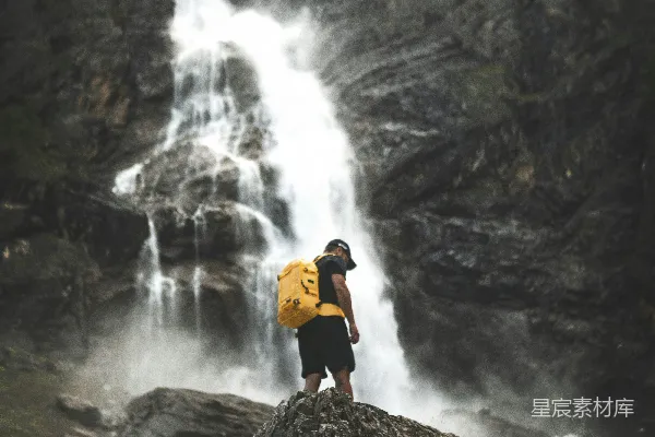 高清摄影 穿橙色夹克的男子站在瀑布附近的岩石上，白天。