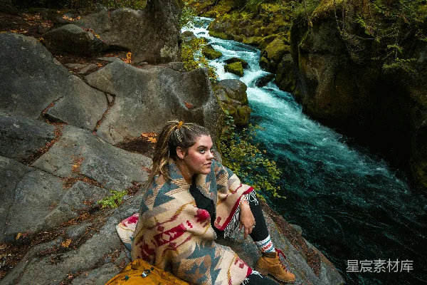 高清摄影 穿着粉红色夹克的女人坐在河边的岩石上。