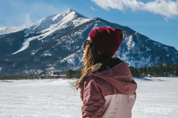 高清摄影 一位女士坐在雪地里，背景是山。