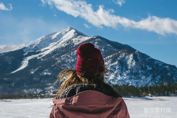高清摄影 一个女人站在雪地里，背景是一座山。