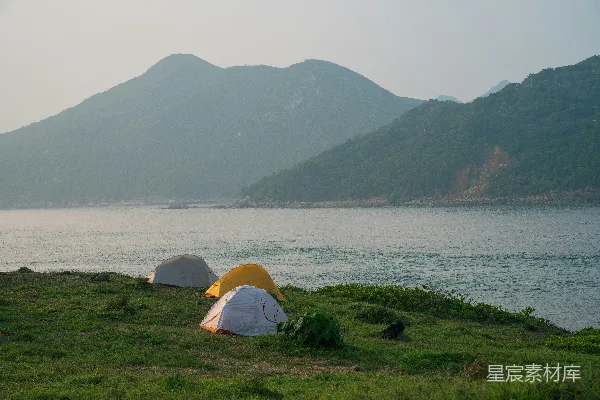 高清摄影 在沿海的小山上搭建露营帐篷，周围是山脉和大海。