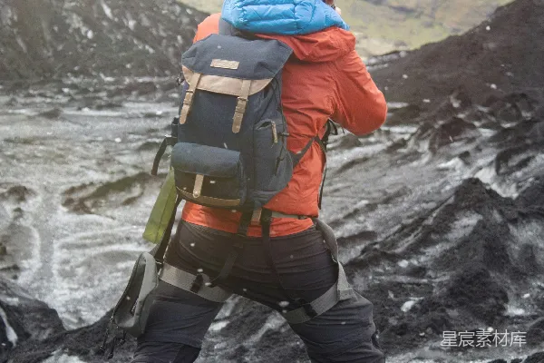 高清摄影 穿橙色夹克和黑色裤子，背着黑色背包的男人在白天走在岩石路上。