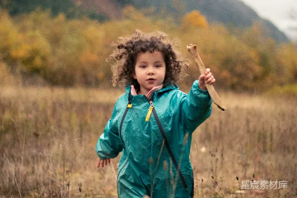 高清摄影 一个穿着绿色雨衣的小女孩手里拿着一根棍子