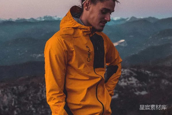 高清摄影 一个穿着黄色夹克的男人站在山顶上。