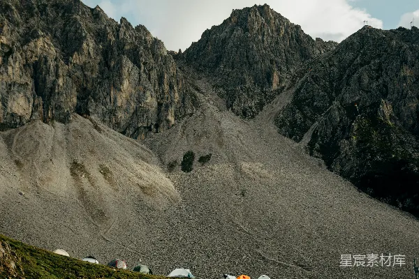 高清摄影 帐篷沿着草地山丘排列，背景是岩石山峰。