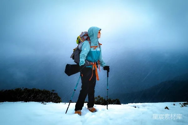 高清摄影 一名徒步者站在雪地里，背着背包，手拿登山杖。