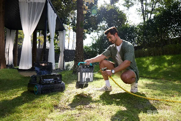 高清摄影 男人在花园里给一台自动割草机浇水。