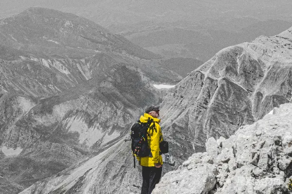 高清摄影 穿着黄色夹克和黑色裤子的人站在覆盖着积雪的山地上。