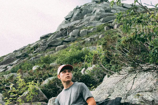 高清摄影 年轻男子坐在岩石上，抬头望向远处的山峦。