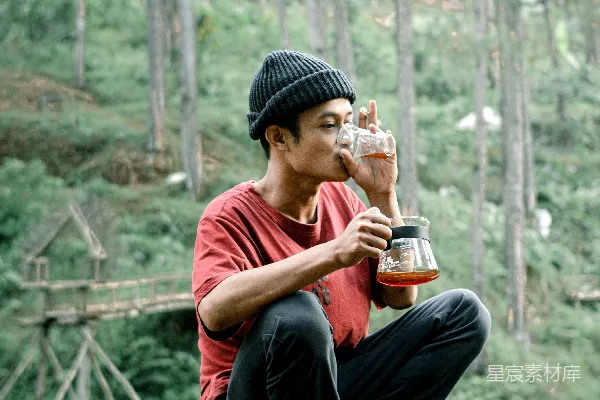 高清摄影 一个男人坐在岩石上，从瓶子里喝水。