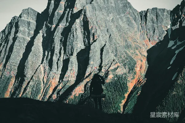 高清摄影 一个人站在绿色的草地上，背景是棕色的岩石山，时间是在白天。