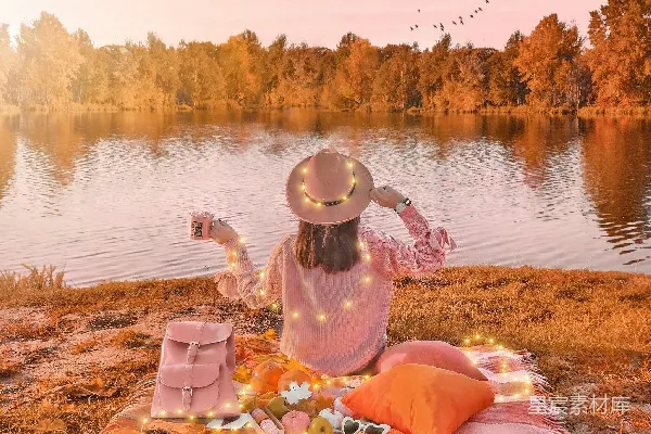 高清摄影 在夕阳下，一个女人在平静的湖边野餐。