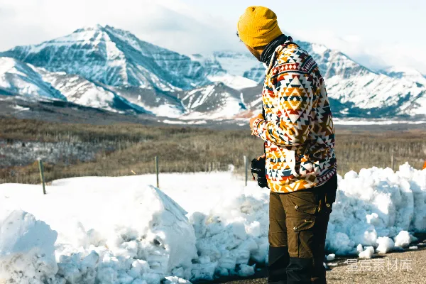 高清摄影 一个男人站在被雪覆盖的山脉前的公路上。
