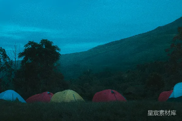 高清摄影 黄昏时分，草地上有多个露营帐篷，远处是山。