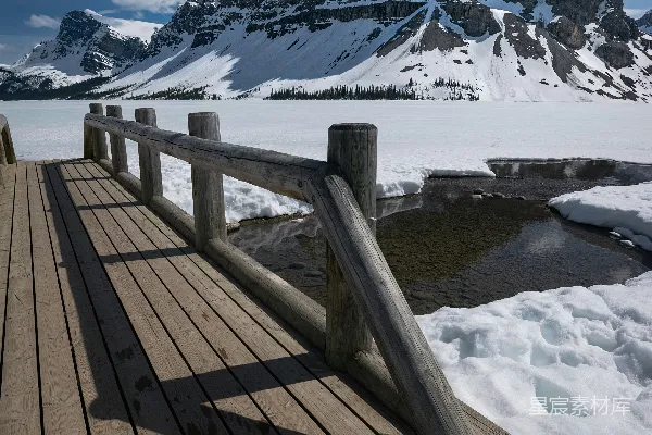 高清摄影 一座木桥横跨水面，背景是被雪覆盖的山脉。