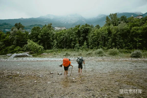 高清摄影 背着背包的徒步者穿过浅浅的河流，向山脉走去。