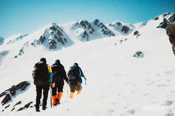 高清摄影 三名徒步旅行者在晴朗的天空下攀登着被雪覆盖的山峰。