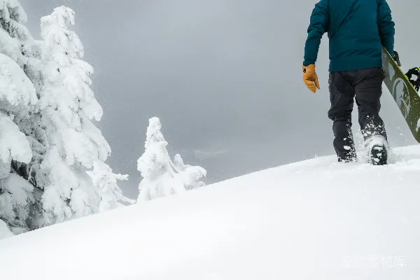 高清摄影 一个男人正背着滑雪板走在被雪覆盖的山上。