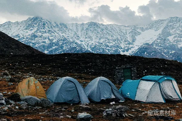 高清摄影 帐篷搭在岩石地面上，背景是雪山。