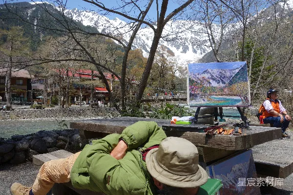 高清摄影 男人在画架旁睡觉，画架上有山景画。