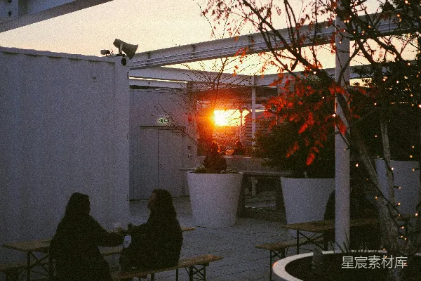 高清摄影 两个人坐在屋顶露台的桌子旁，夕阳西下。