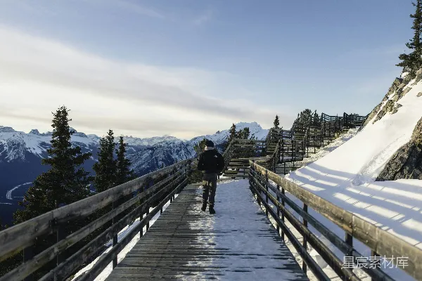 高清摄影 一个人在雪地栈道上行走，背景是山脉景色。
