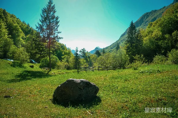 高清摄影 草地开阔地，有一块大石头和森林覆盖的山丘。
