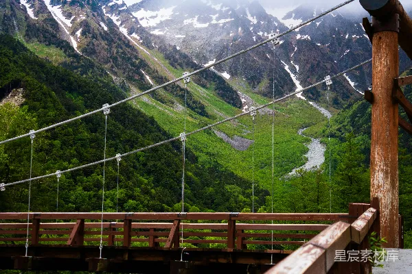高清摄影 一座横跨河流的木制悬索桥，背景是雪山。