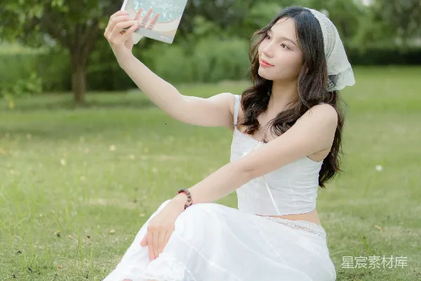 高清摄影 一个女人坐在草地上，手里拿着一本书。