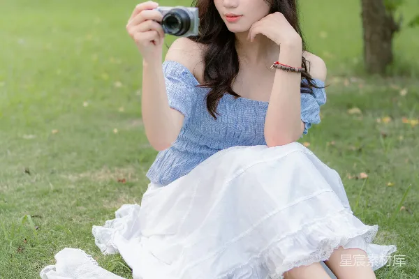 高清摄影 一个女人坐在草地上，手里拿着相机。