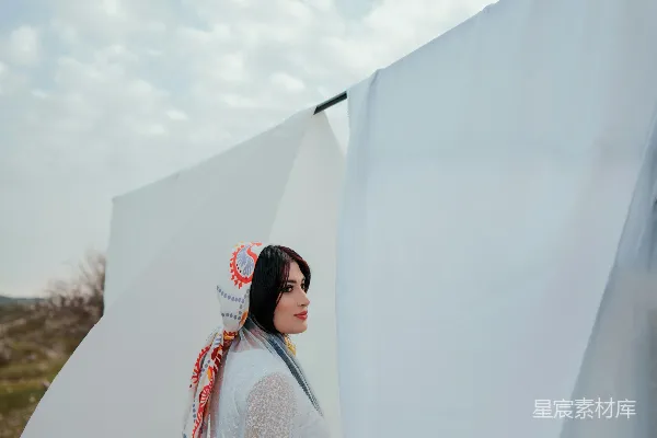 高清摄影 一个穿着白色连衣裙的女人站在一张白色的床单旁边。